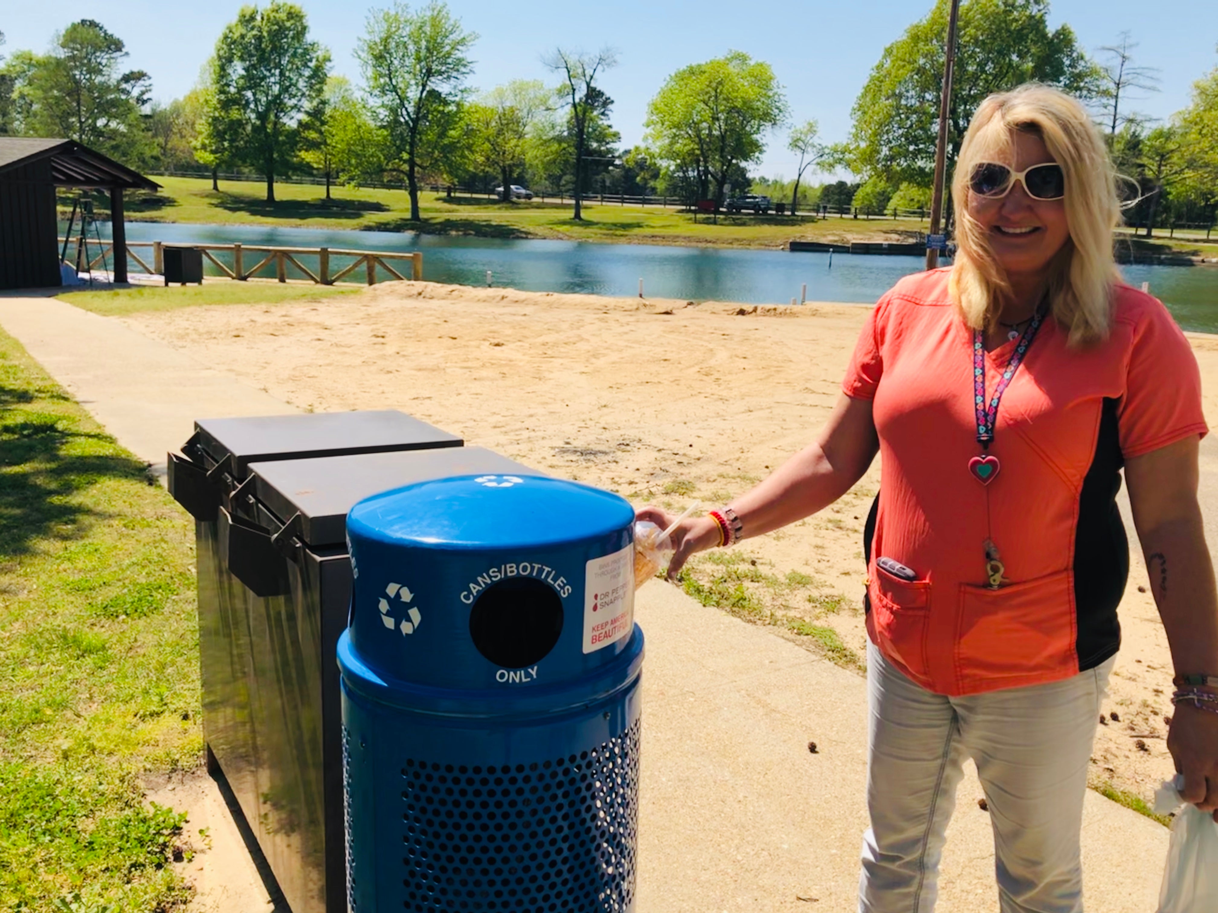 Female staff member dropping a plastic cup into a blue recycling bin after finding it at Lake Ponder beach 